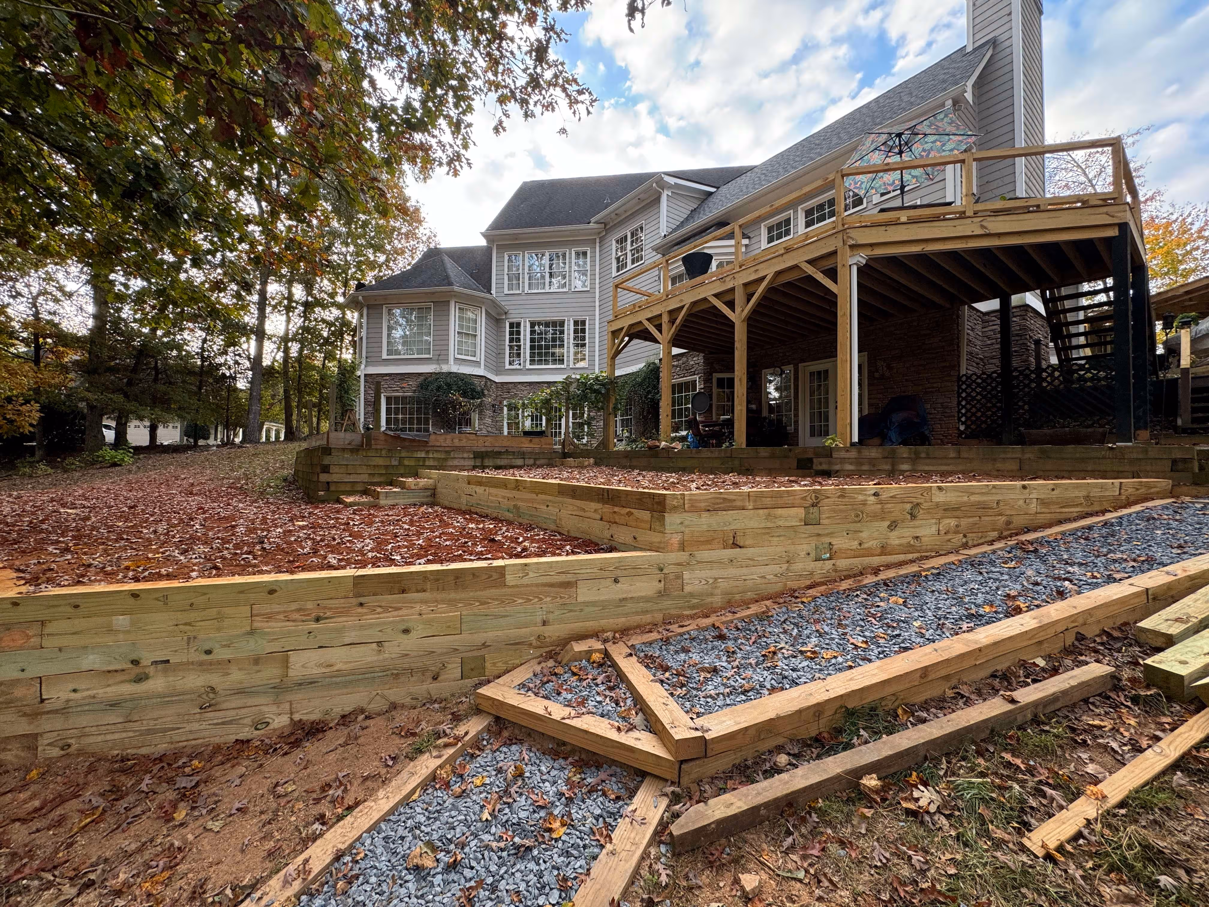multi layer timber retaining wall with gravel walkway and home with back deck in background