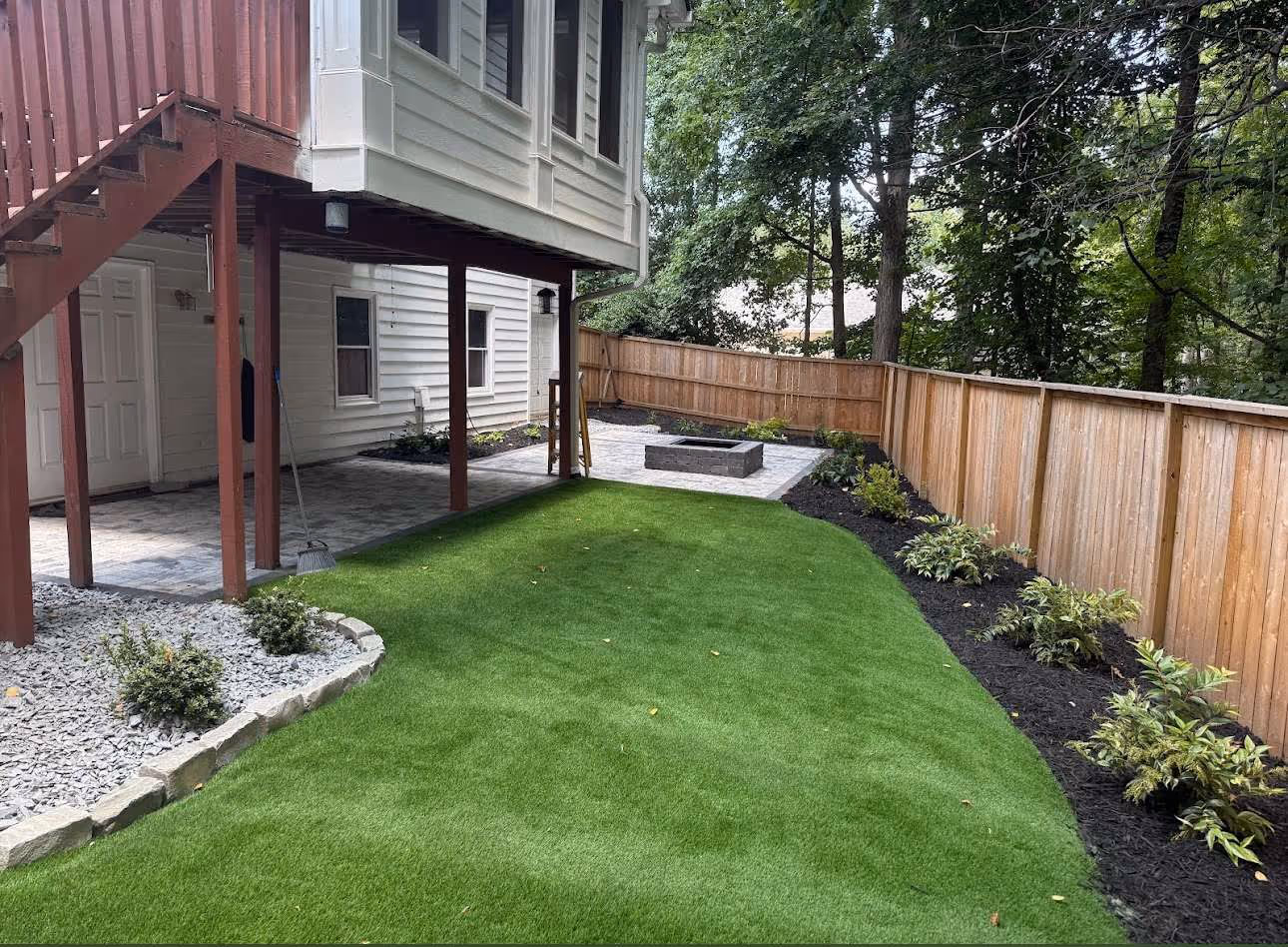 artificial turf lawn with plants surrounding it and fence in background