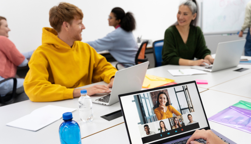 People in an office working on laptops with one laptop showing a video conference call.