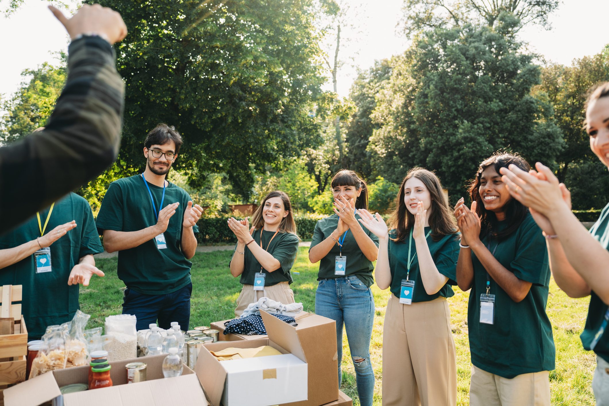 Group of volunteers outdoors clapping near tables with food and supply boxes.