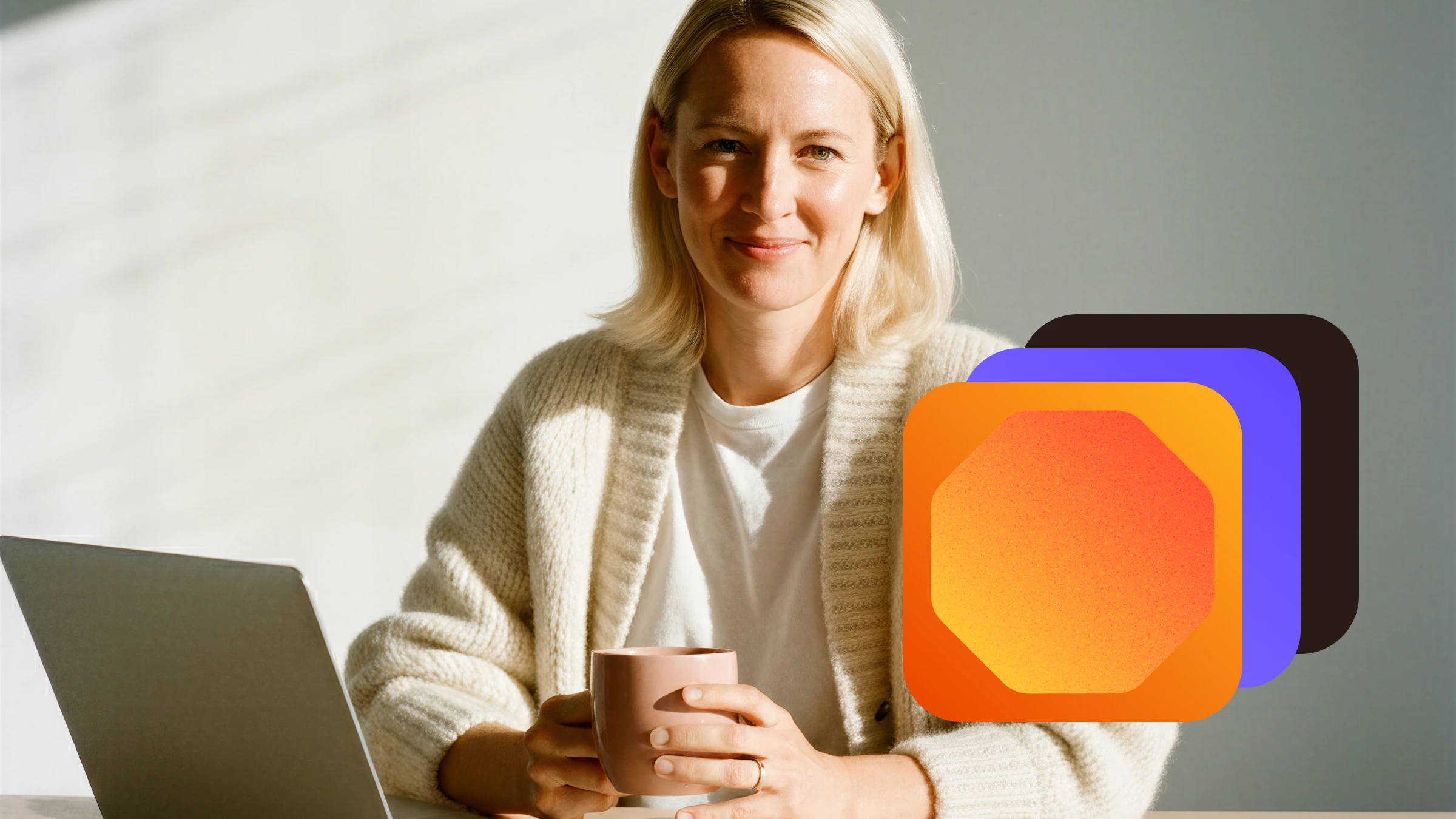 Smiling woman with blonde hair wearing a white sweater, sitting at a table holding a pink mug with a laptop and colorful layered octagonal shapes next to her.