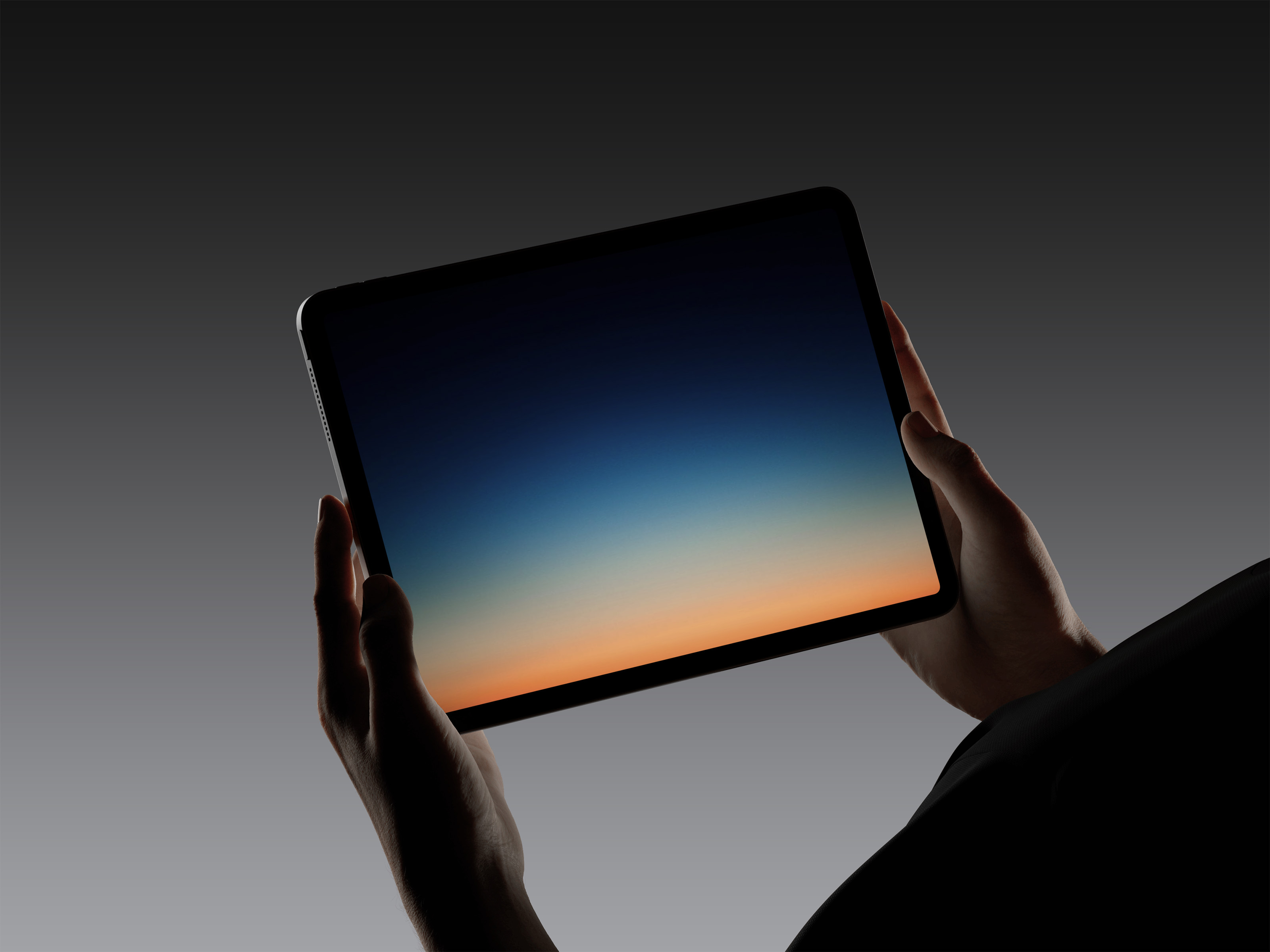 Hands holding a tablet device displaying a gradient screen from dark blue to orange on a dark gray background.