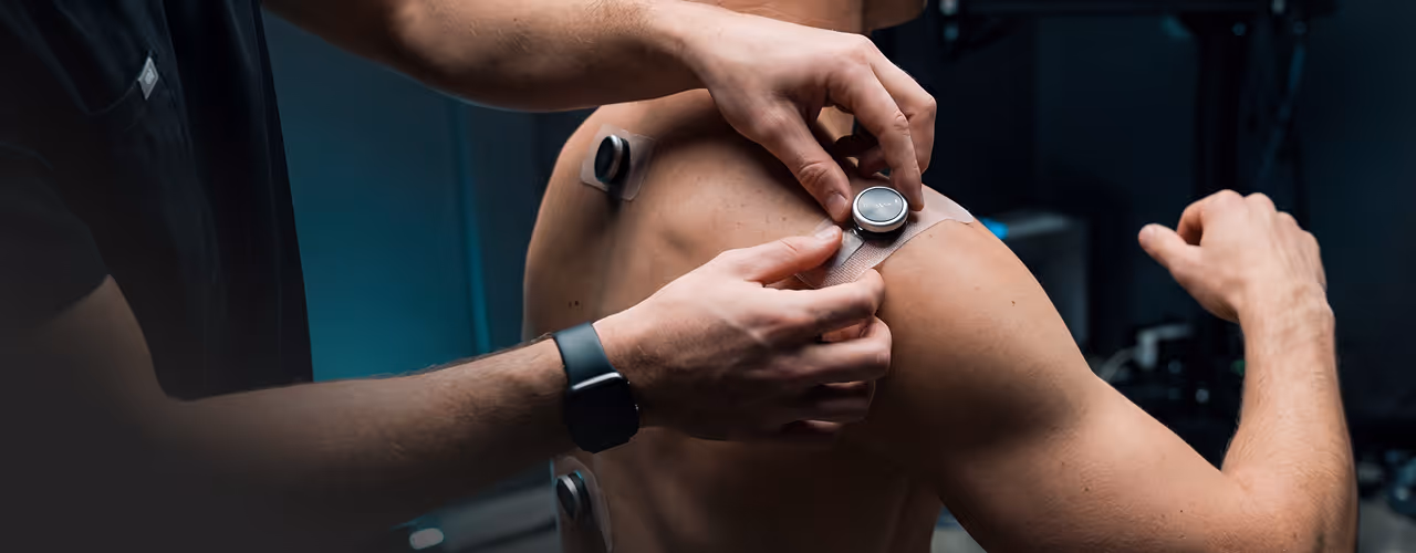 Pessoa aplicando sensor adesivo em ombro de homem sem camisa para monitoramento da saúde.