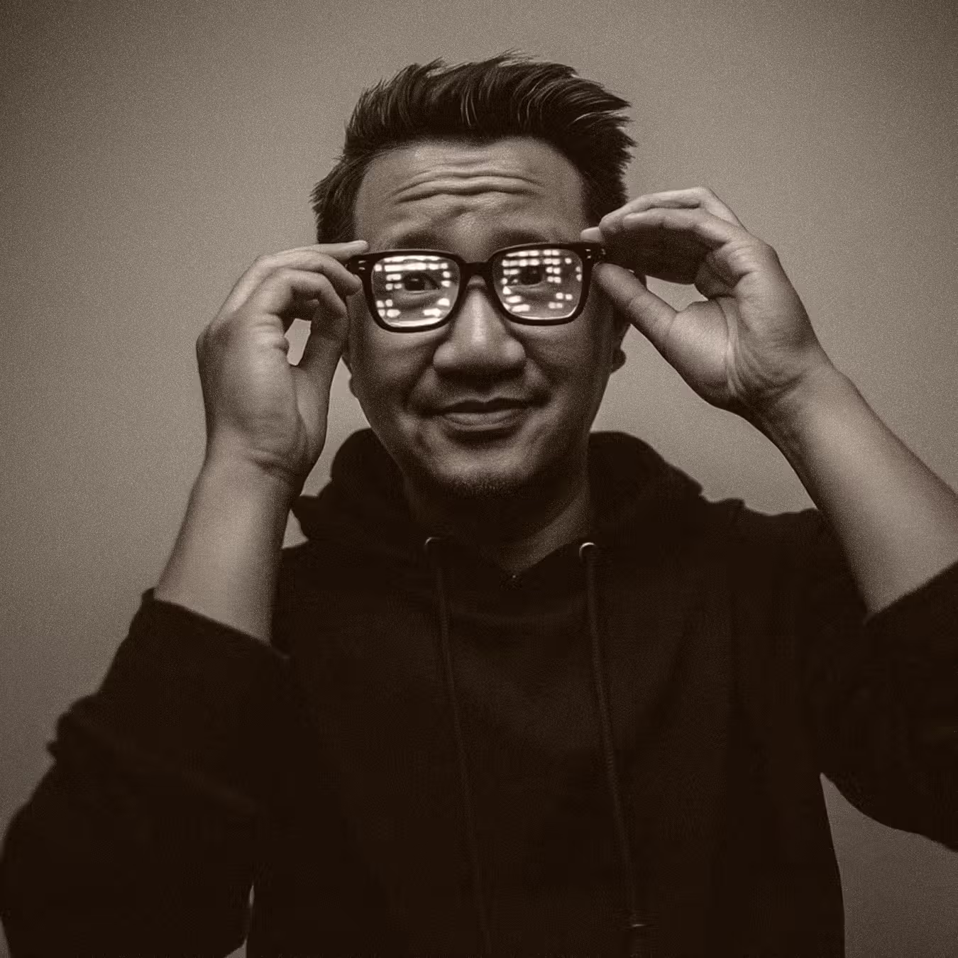 Man wearing glasses with light reflections, adjusting frames with both hands, smiling slightly.