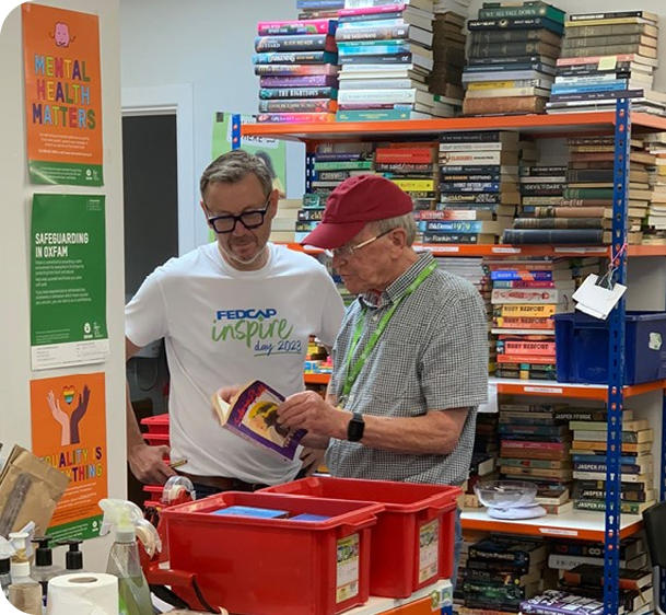Two men sort donated items into boxes in a room lined with bookshelves.