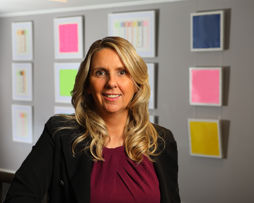 Susan Paterson, Executive Director of Fedcap, sits for a portrait in an office with colourful framed artwork on the wall behind her.