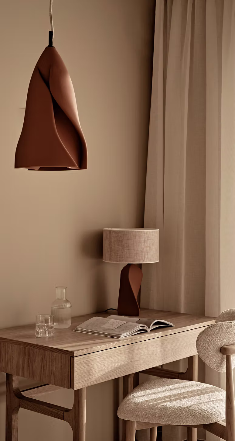 Minimalist wooden desk with an open book, glass water set, fabric lamp, and a unique pendant light hanging above.