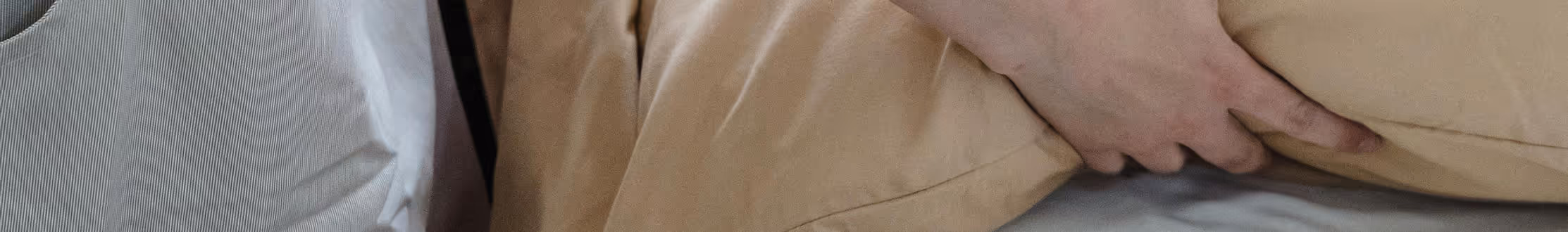 Hand gently holding a beige pillow on a bed with white and beige bedding.