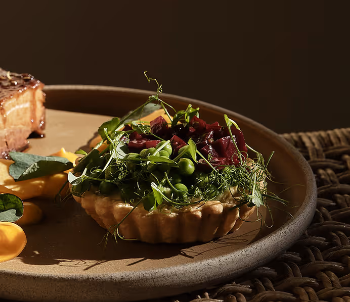 Savory tart topped with green peas, pea shoots, and diced red beets on a brown ceramic plate.
