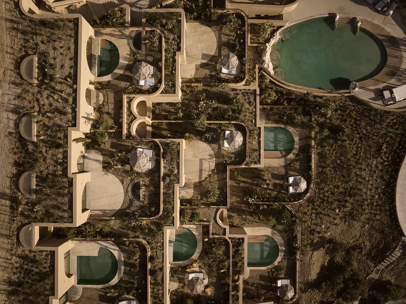 Top-down aerial view of a luxury resort with beige walls, multiple small private pools, shaded lounging areas, and greenery.