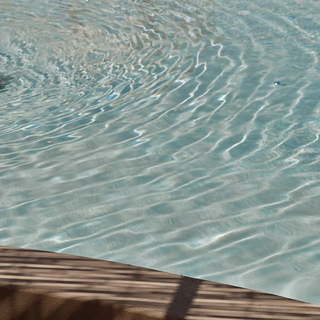 Close-up of rippling water surface with pool edge and shadows of slats.
