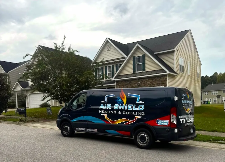 Dark blue Air Shield Heating & Cooling service van parked on a residential street in front of light-colored houses.