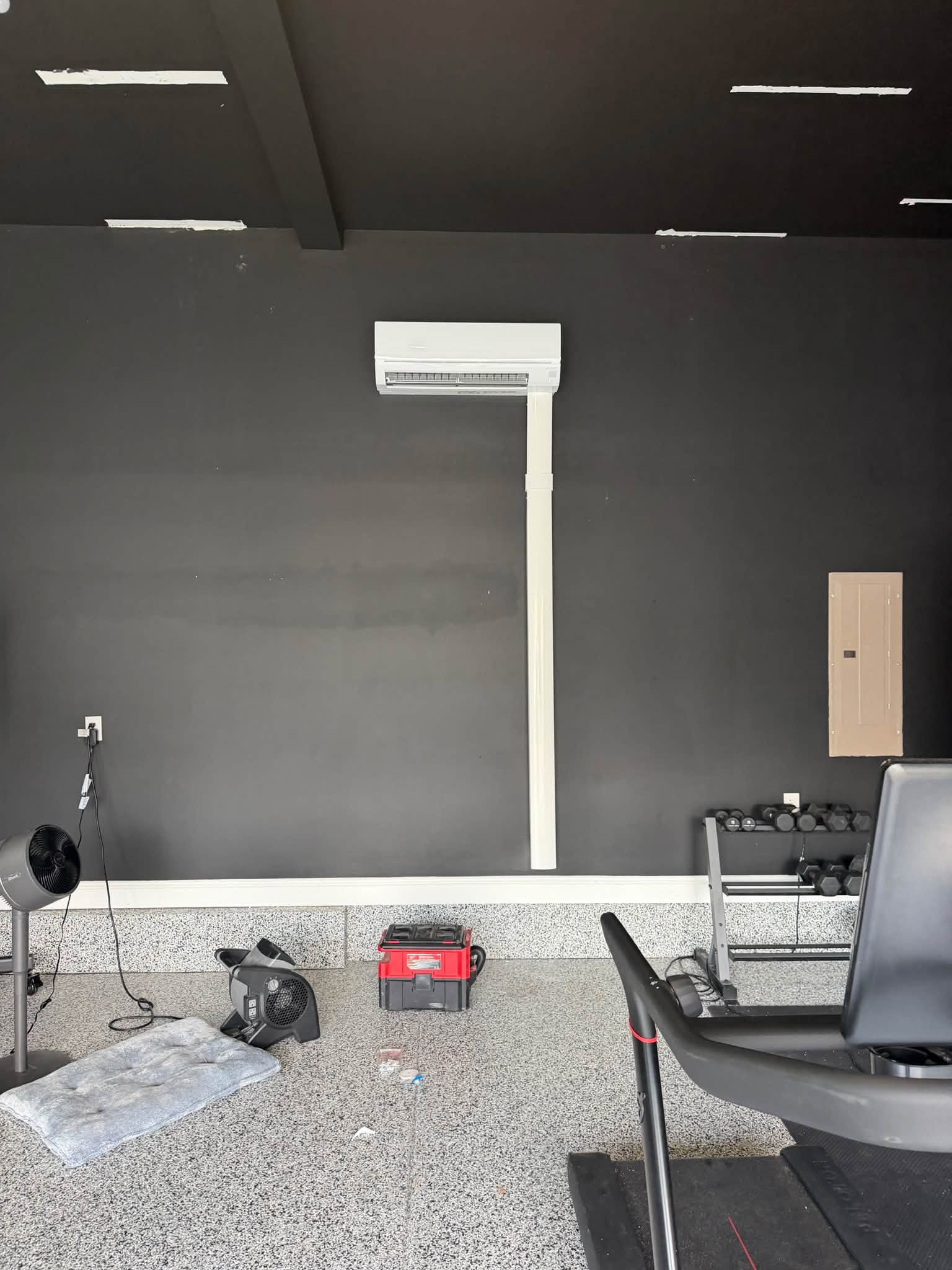 A wall-mounted ductless mini-split AC unit installed on a dark wall inside a home gym in Holly Springs, NC.