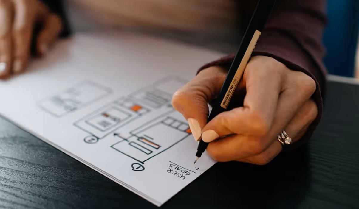 Close-up of a person writing on a paper flowchart or diagram with sections and labels, including a note labeled 'User Goals.'