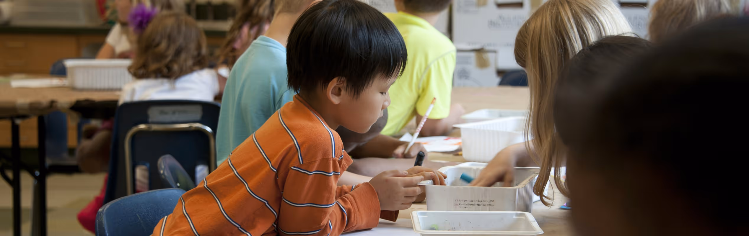 Children sitting at a table in a classroom engaged in arts and crafts activities.