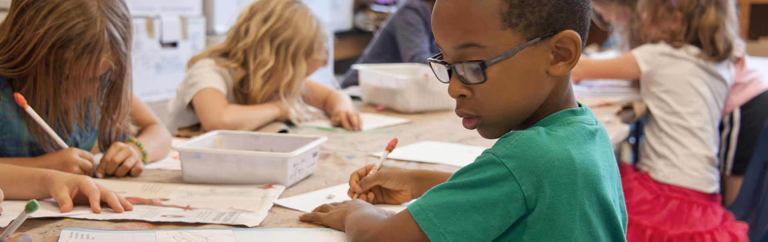 A diverse group of young children focused on drawing and writing at a classroom table.