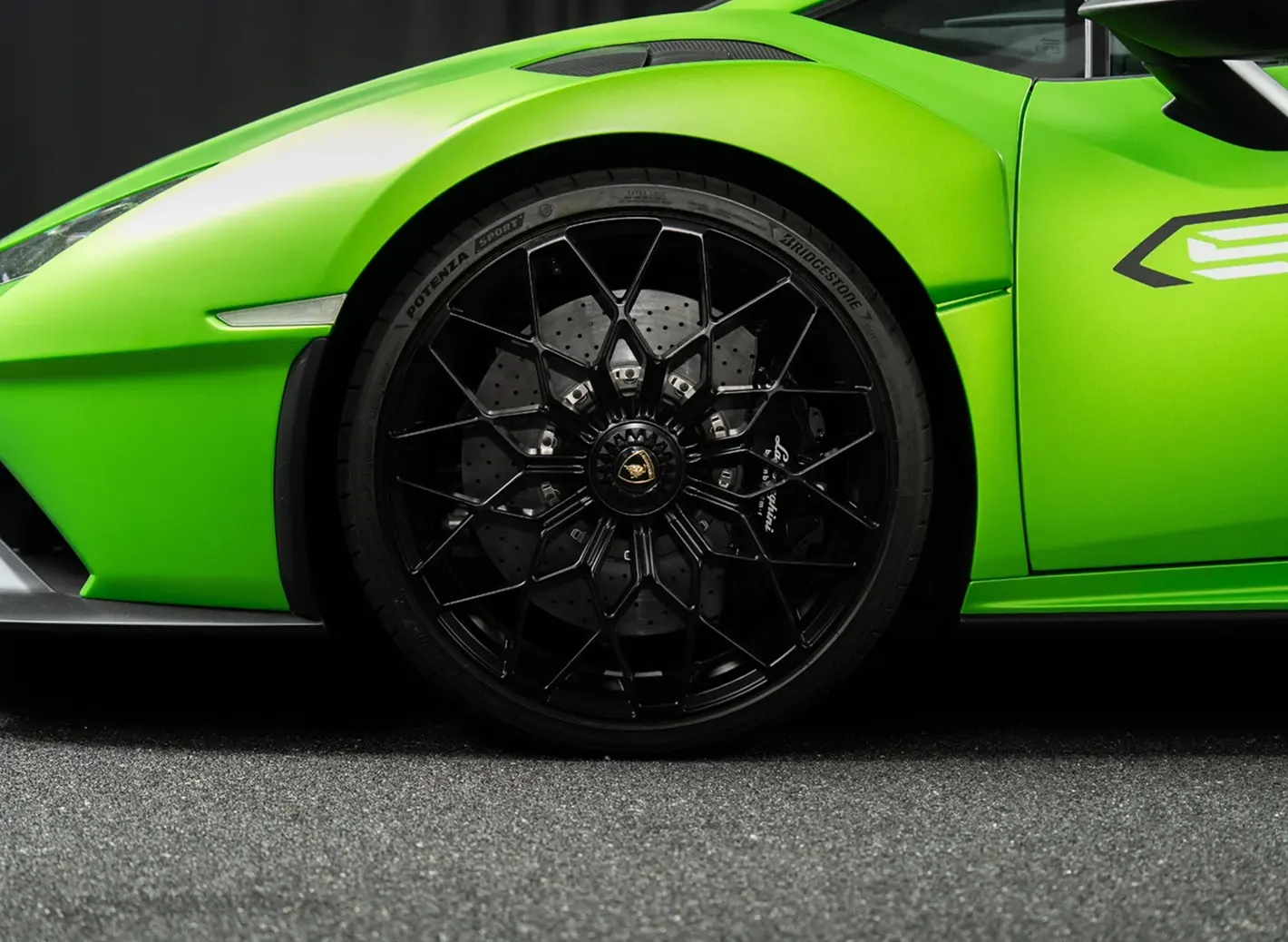 Close-up of a black multi-spoke wheel and tire on a bright green Lamborghini sports car.