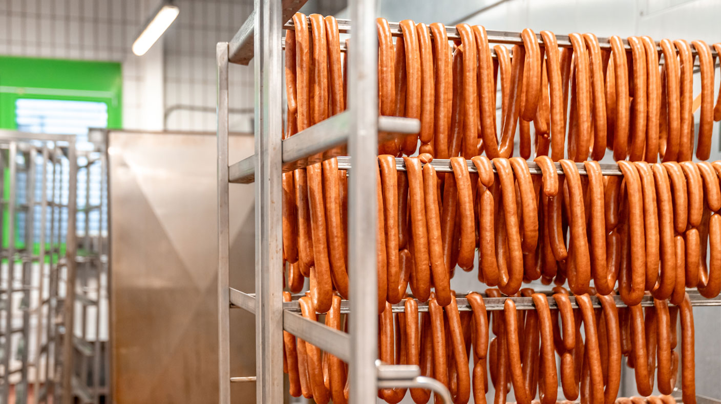 Worker in white coat and blue gloves placing raw meat into vacuum-sealed packaging in a processing plant.