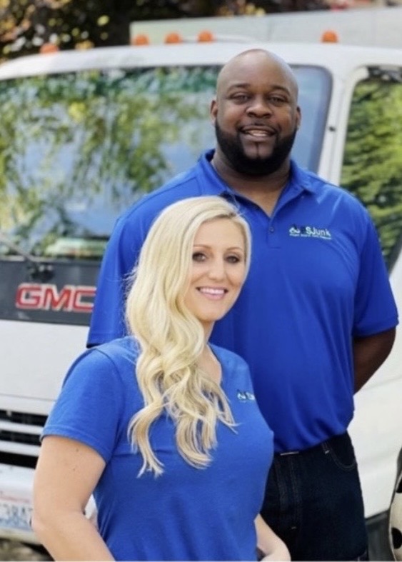 Smiling man and woman in blue shirts standing in front of a white GMC van.