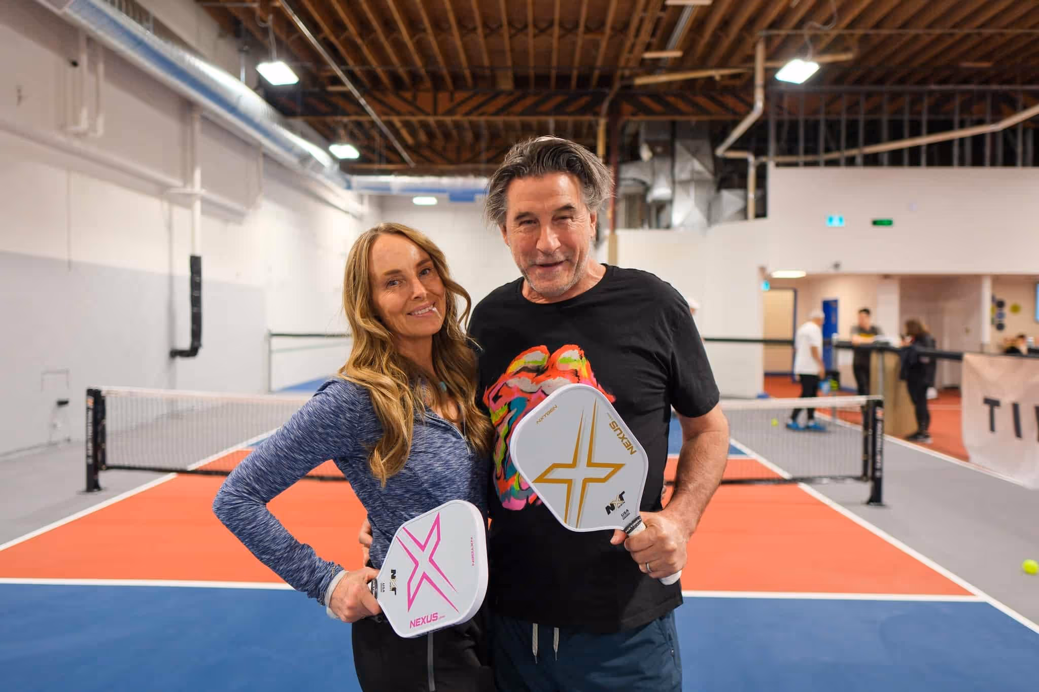 Smiling man and woman holding pickleball paddles on an indoor court.