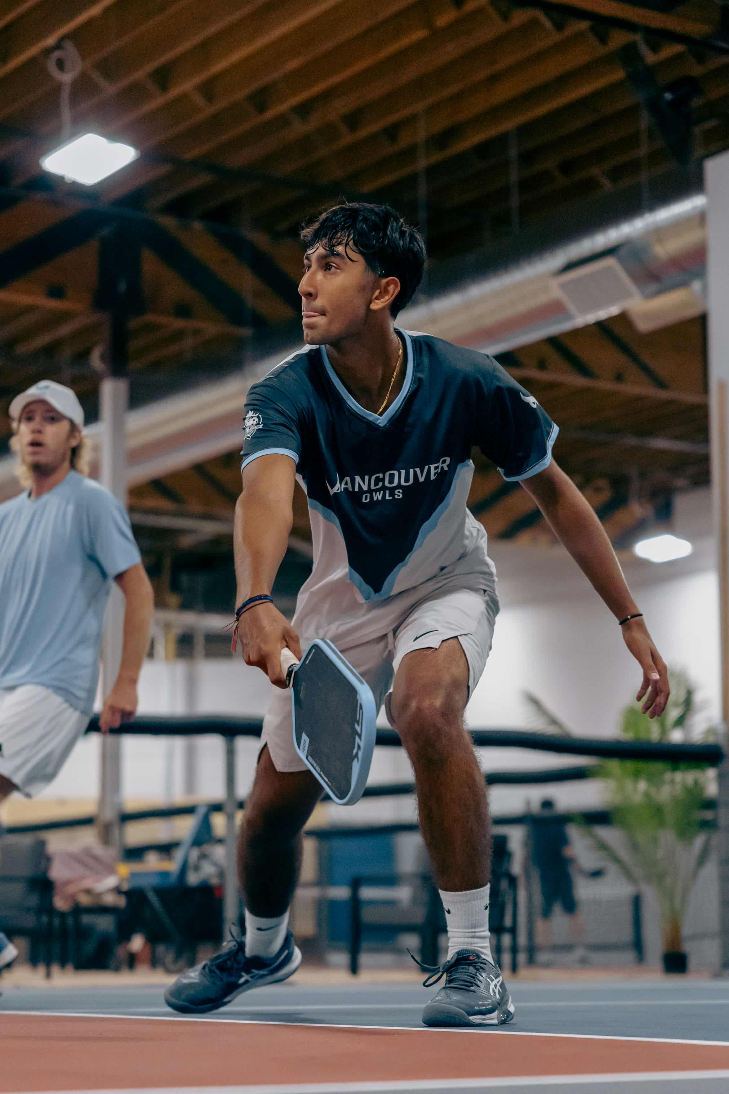 Young man in Vancouver Owls uniform playing indoor pickleball with paddle ready to hit the ball.