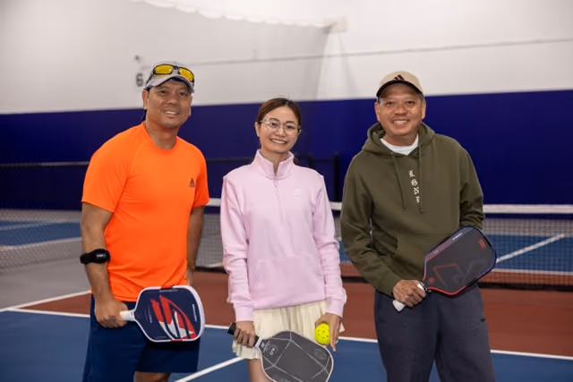 Four women standing together indoors, smiling at the camera with casual and sporty clothing.