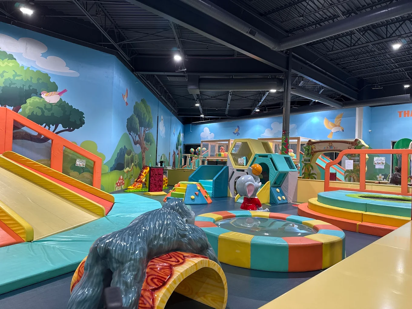 Indoor children's play area with colorful padded slides, climbing structures, and animal decorations.