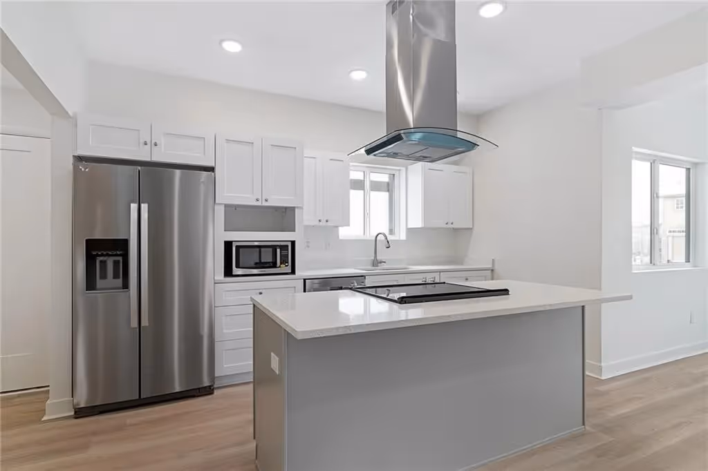 Modern kitchen with white cabinets, stainless steel fridge, island with stovetop, and ventilation hood.