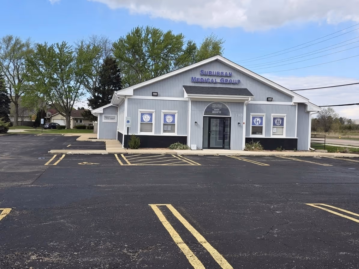 Gray Suburban Medical Group building with parking lot and trees in the background under a partly cloudy sky.
