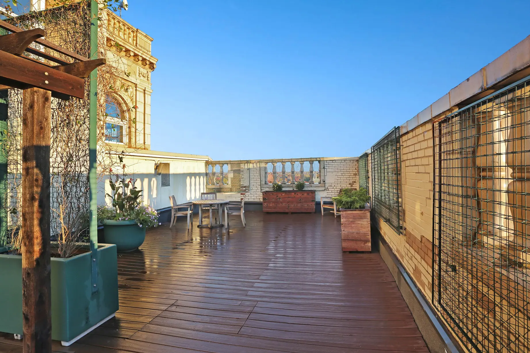 Spacious rooftop patio with wooden deck, outdoor furniture, planters, and clear blue sky.