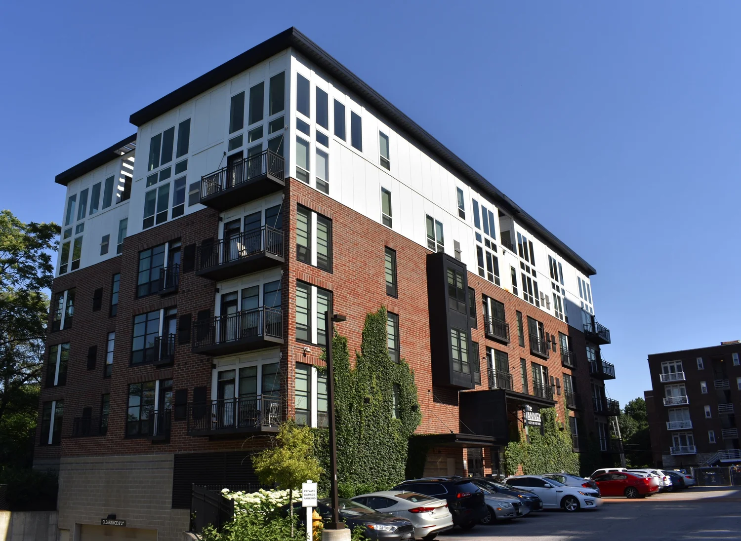 Modern five-story apartment building with brick and white panel exterior and parked cars outside.