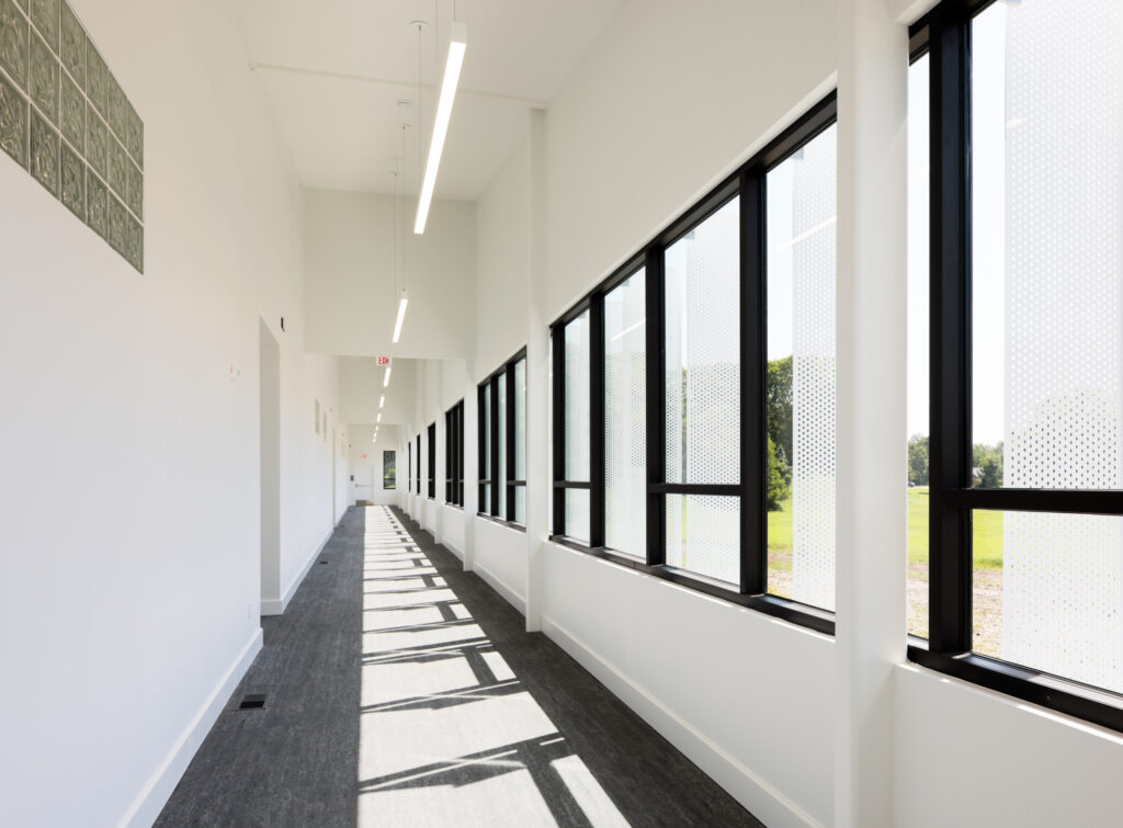 Long bright hallway with large windows on the right casting shadows on the floor.