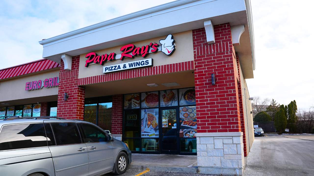 Papa Ray's Pizza & Wings restaurant storefront with a parked silver minivan outside.