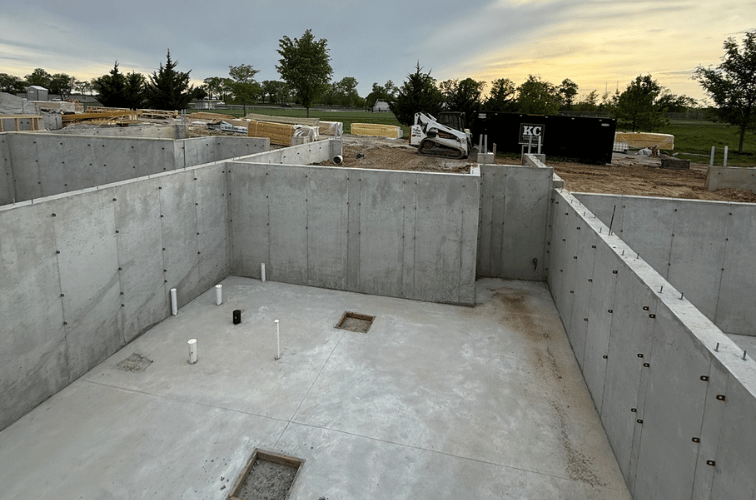Concrete foundation walls and floor of a building under construction with pipes and equipment nearby.
