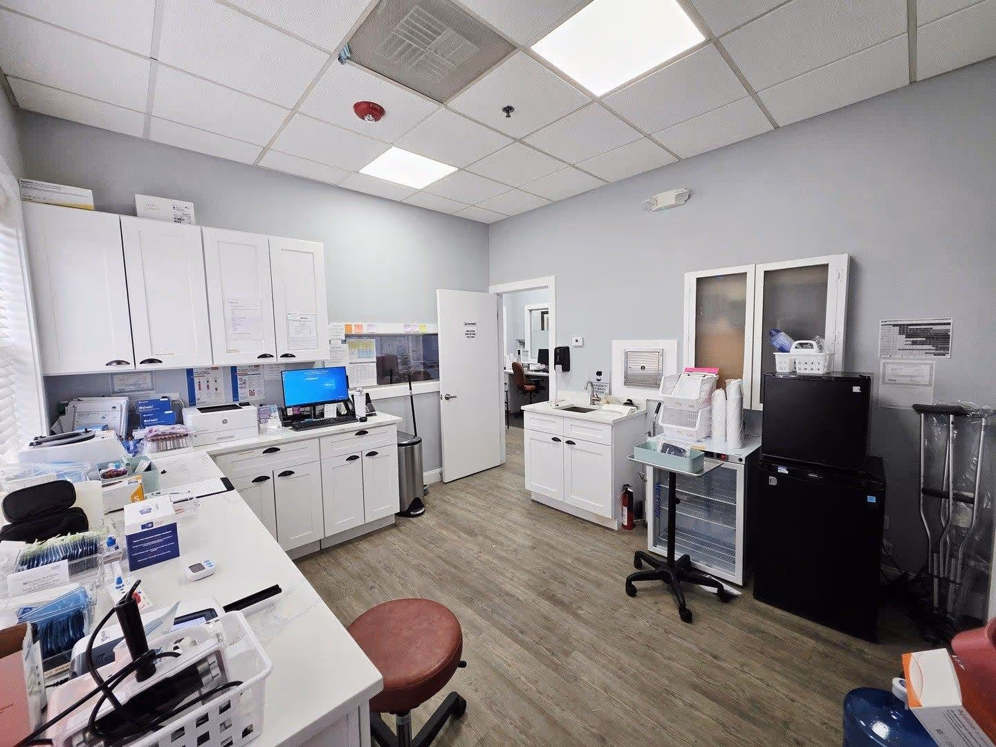 Medical office reception area with a counter window, chair, trash can, and open door to a room with shower.