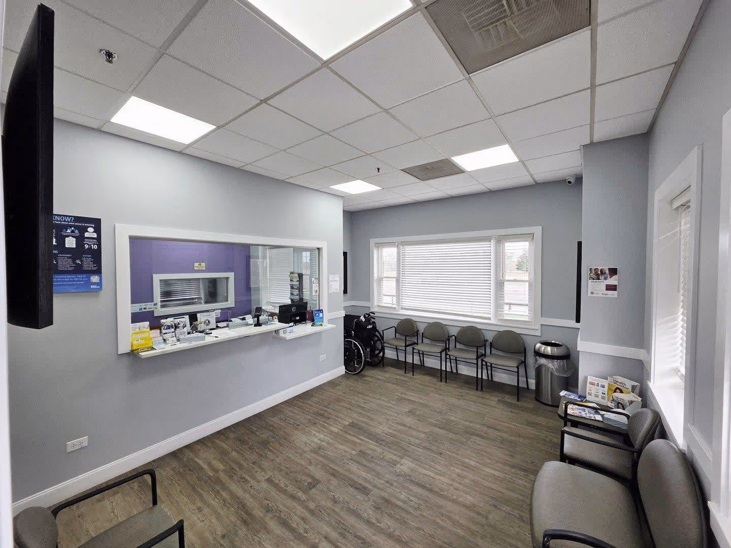 Medical office reception area with a counter window, chair, trash can, and open door to a room with shower.