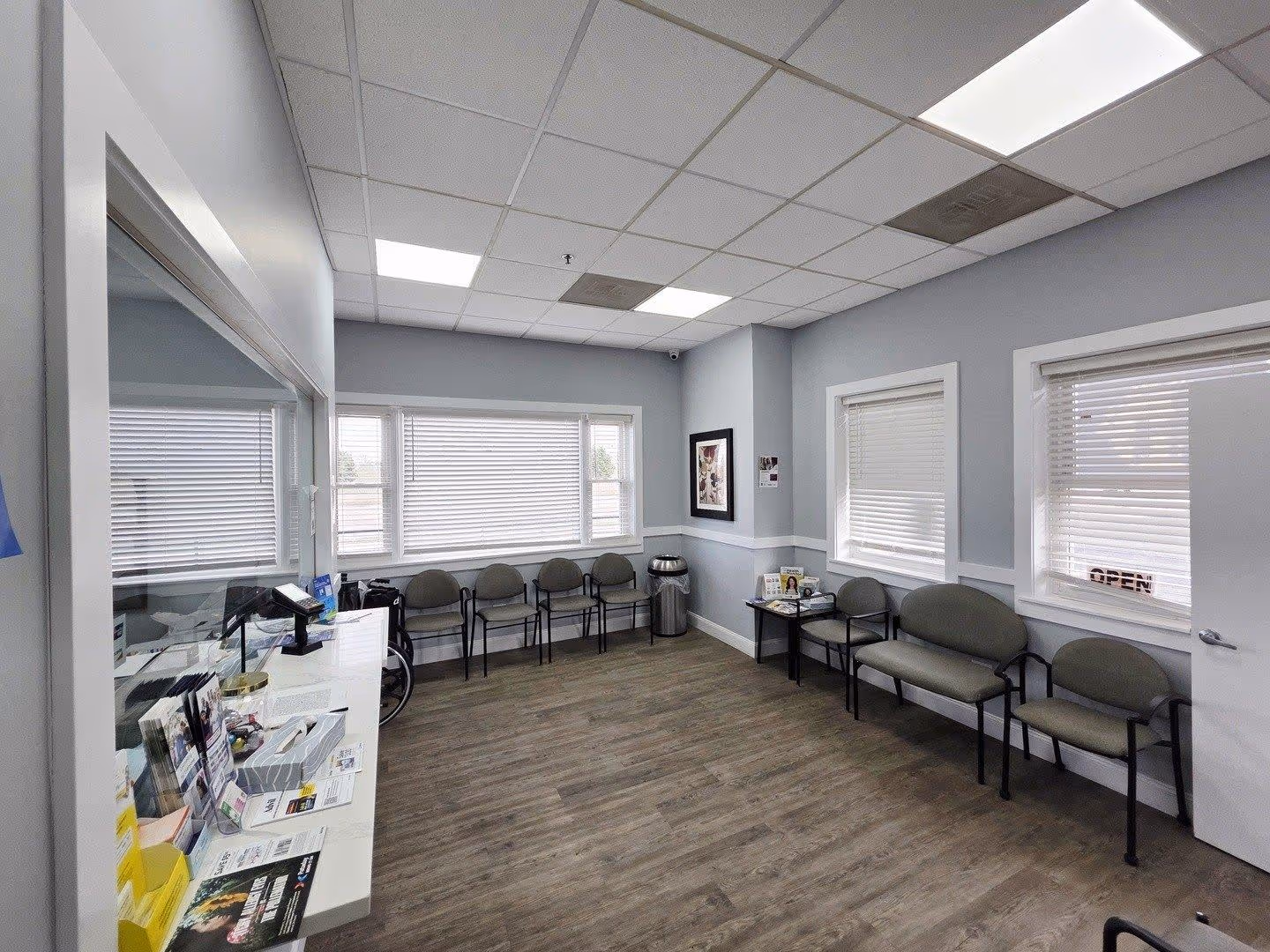 Medical office reception area with a counter window, chair, trash can, and open door to a room with shower.