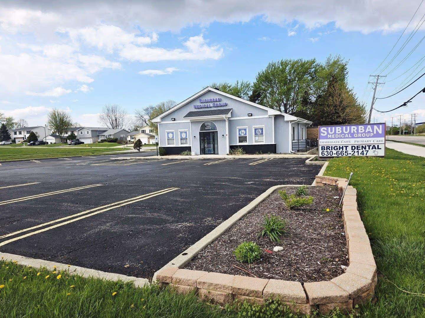 Gray Suburban Medical Group building with parking lot and trees in the background under a partly cloudy sky.