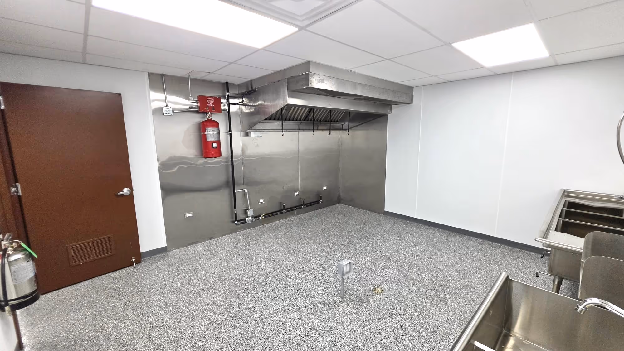 Modern open living space with gray sectional sofa, kitchen with stainless fridge, and dining area by window.