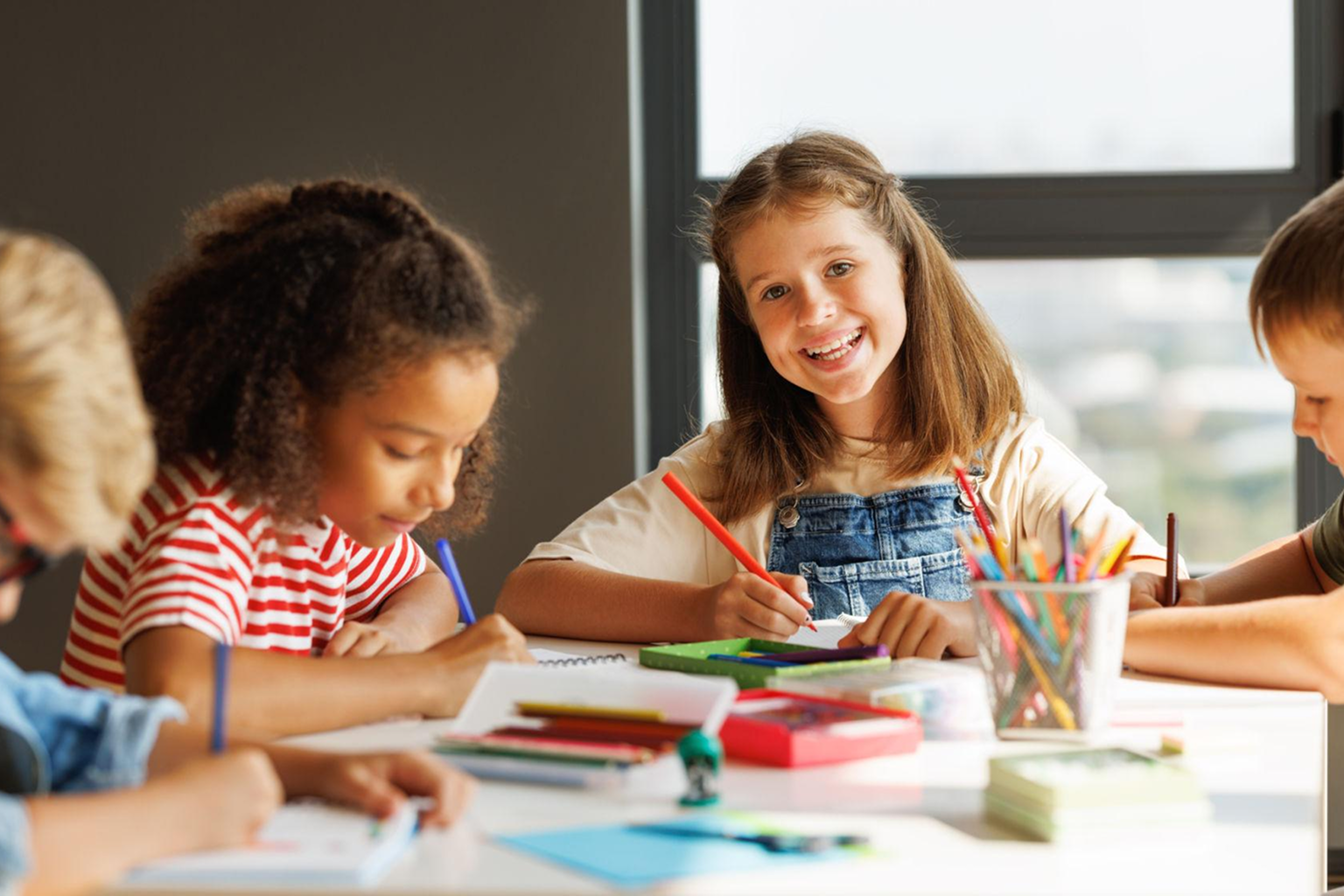 Group of children coloring and drawing at a table with colored pencils and art supplies.