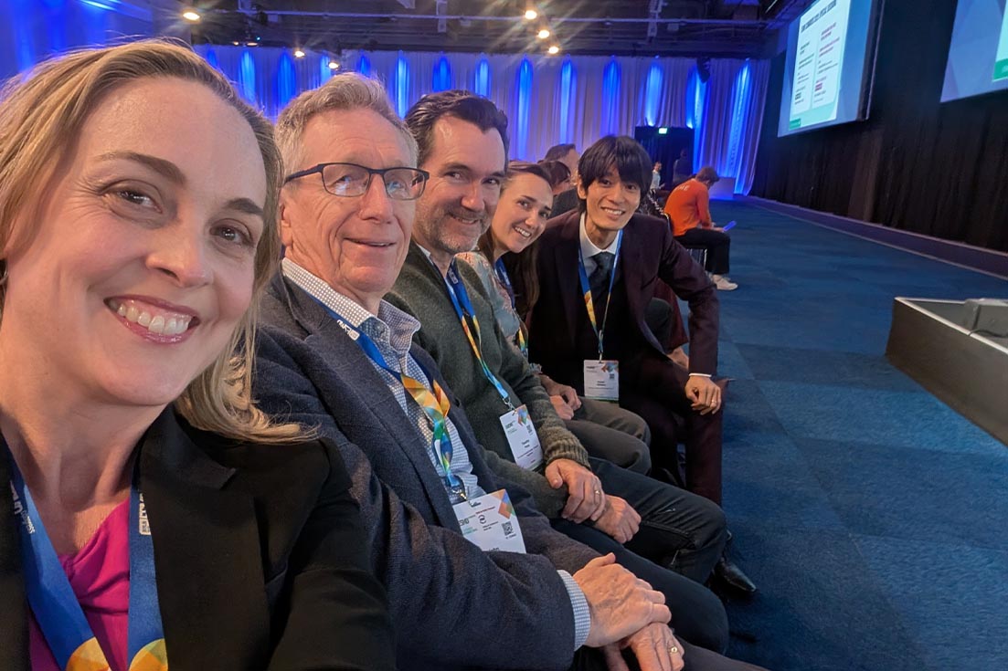A group selfie smiling while seated in the audience of a large conference.