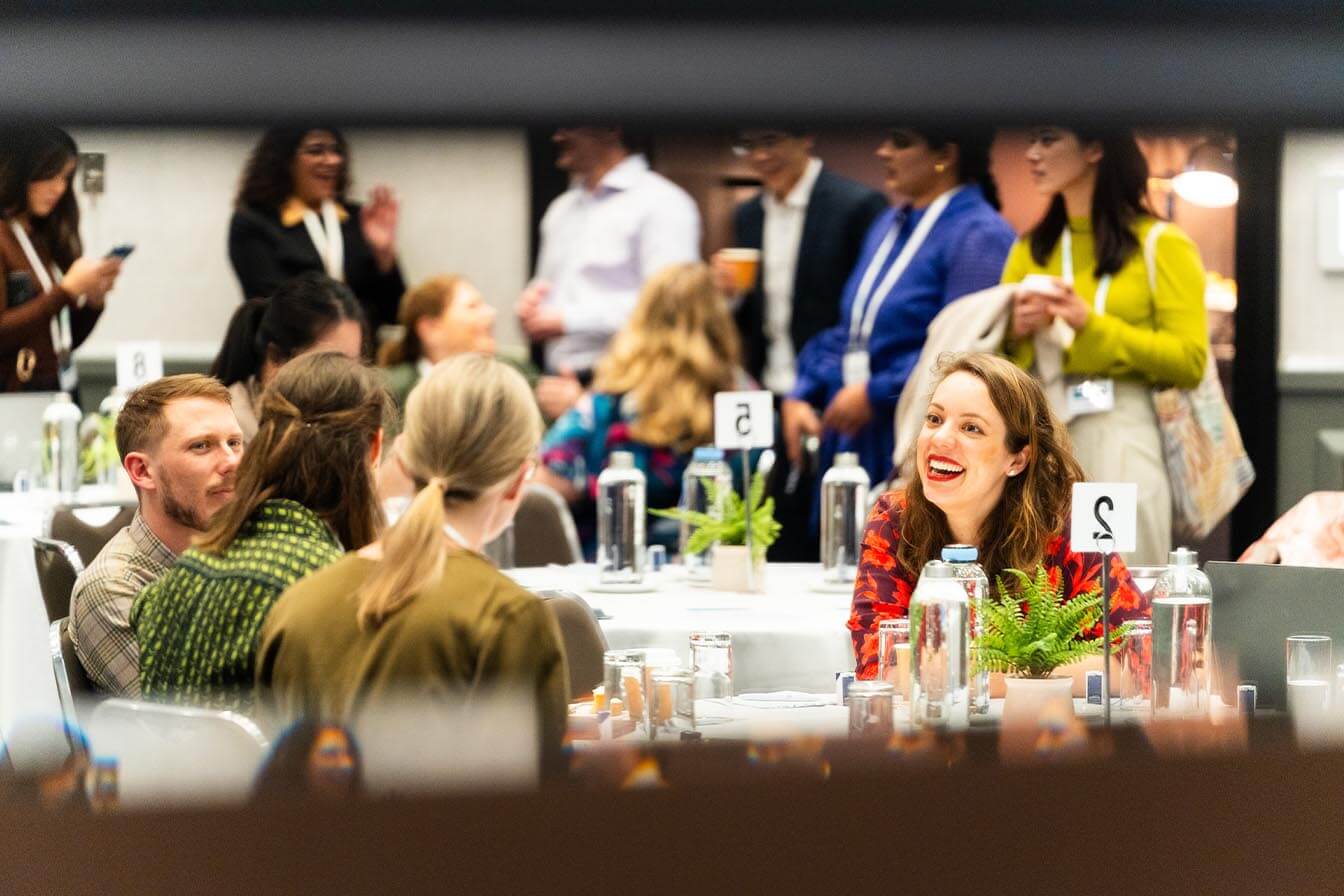 A candid shot of conference attendees networking and laughing around a circular table during a breakout session.