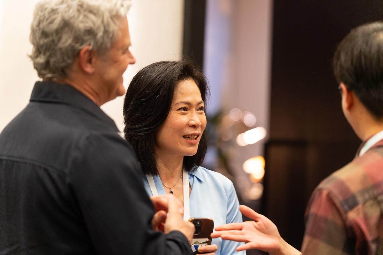 Close-up of woman with dark hair smiling while engaged in a conversation with colleagues during a conference break.