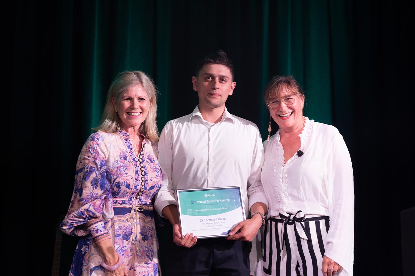 Man holding his award certificate, flanked by two smiling presenters