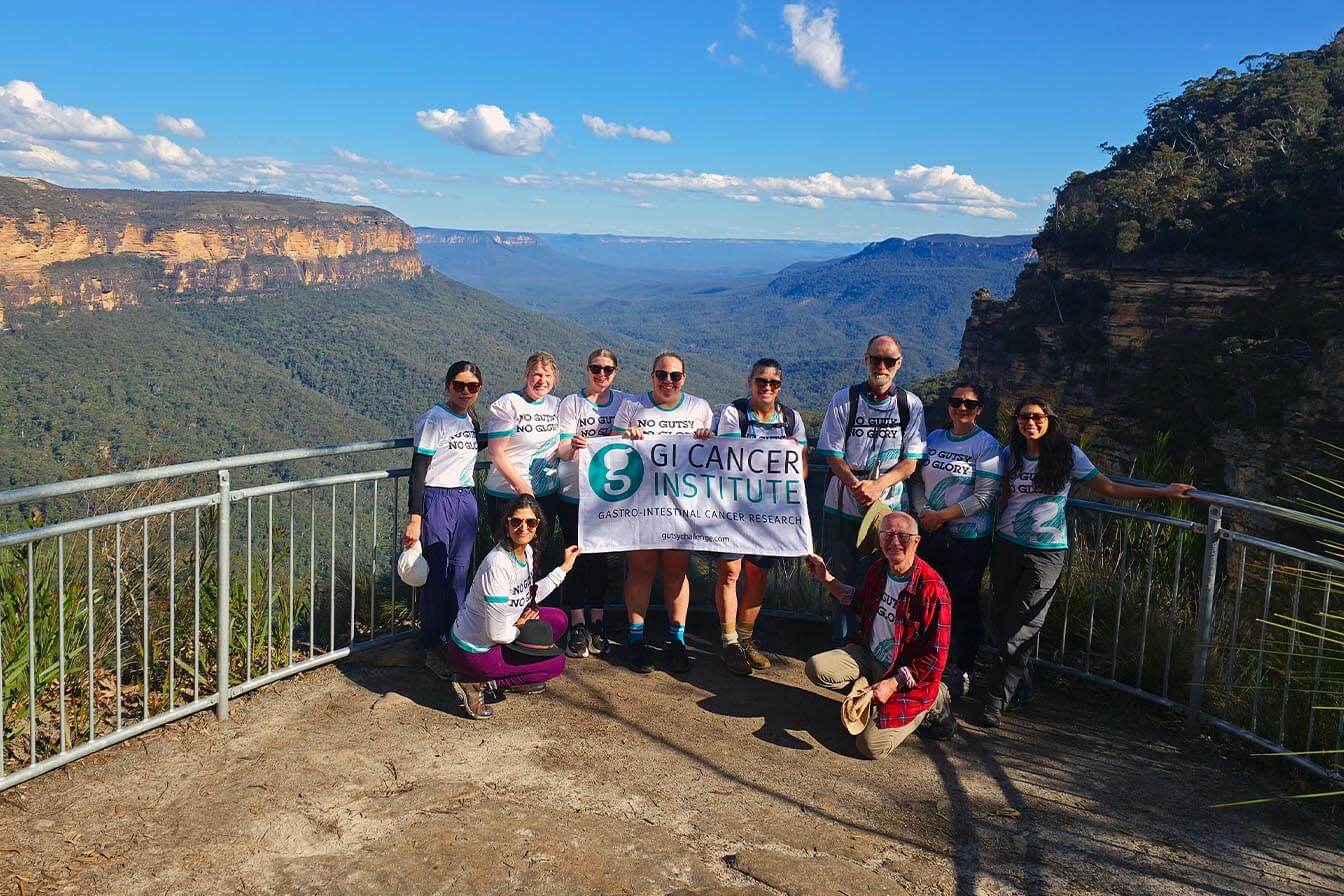 A group of hikers holding a GI Cancer Institute banner at a scenic lookout in the Blue Mountains.