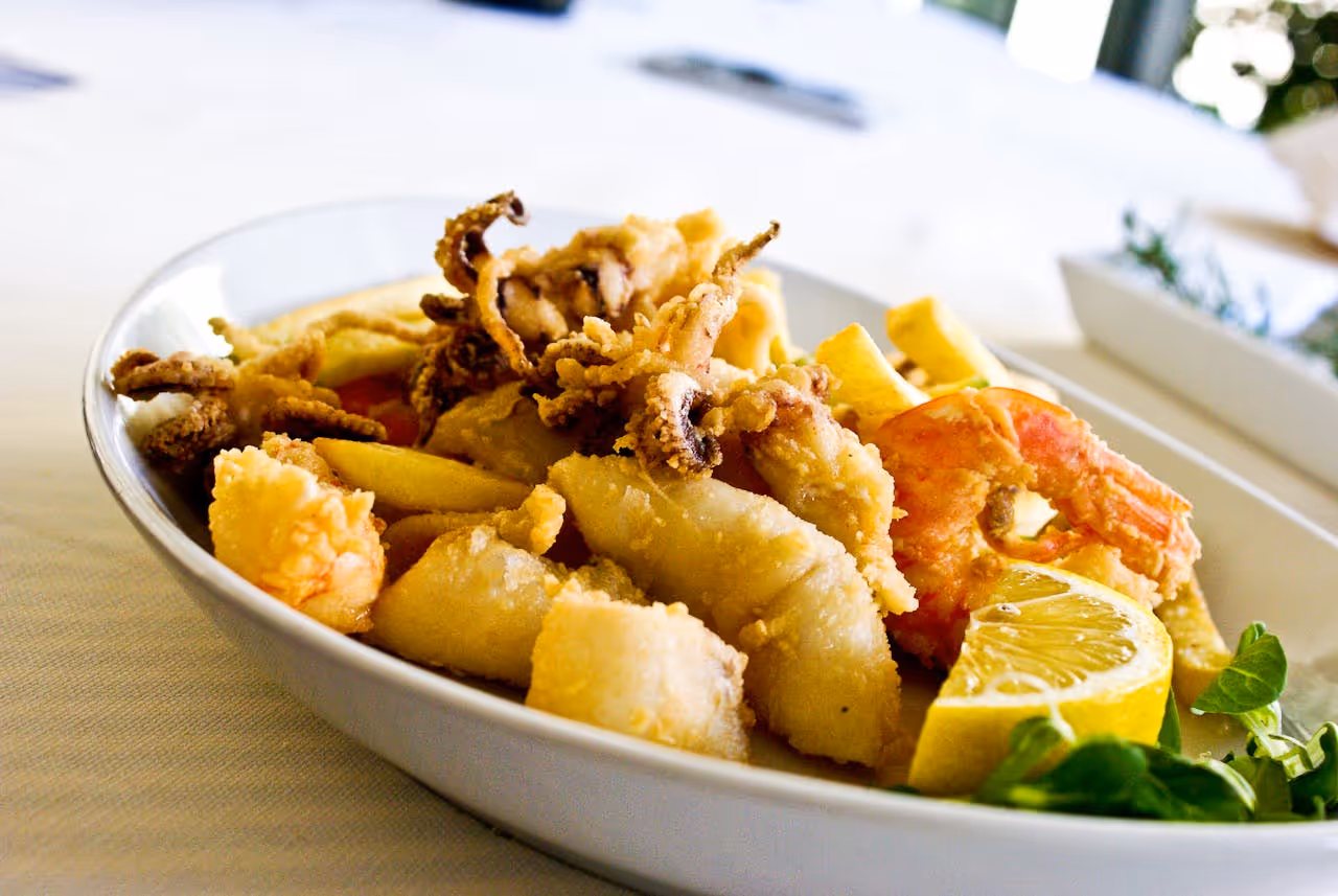 Plate of fried seafood with shrimp, calamari, and lemon wedge garnished with greens.
