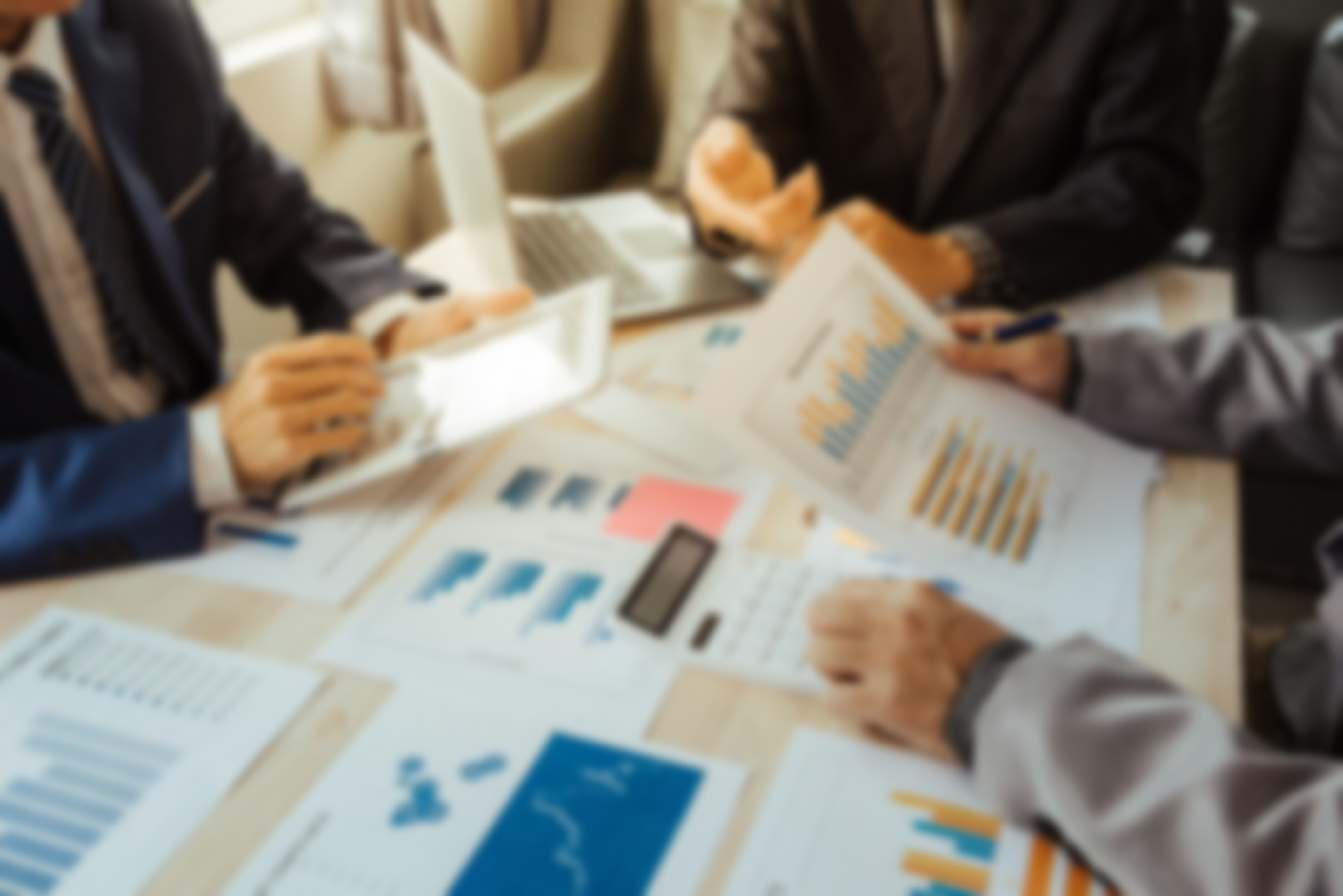 Business meeting with three professionals discussing charts and graphs spread on a table, using a tablet and a calculator.