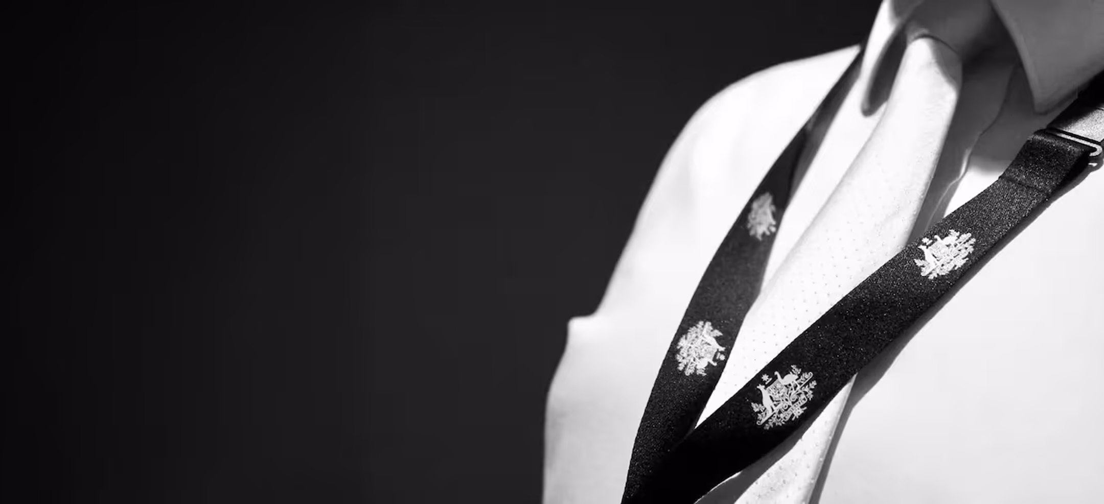 Close-up of a person wearing a white shirt and tie with a black lanyard featuring Australia coat of arms design.
