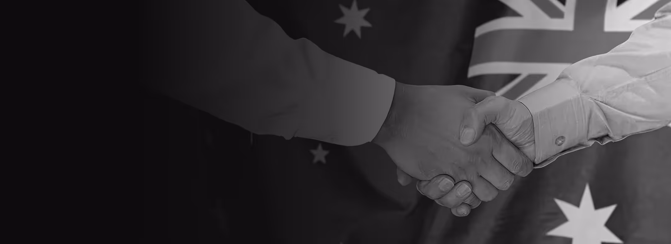 Two people shaking hands with an Australian flag in the background.