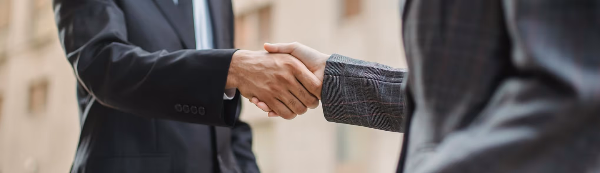 Two people in suits shaking hands in a professional setting.